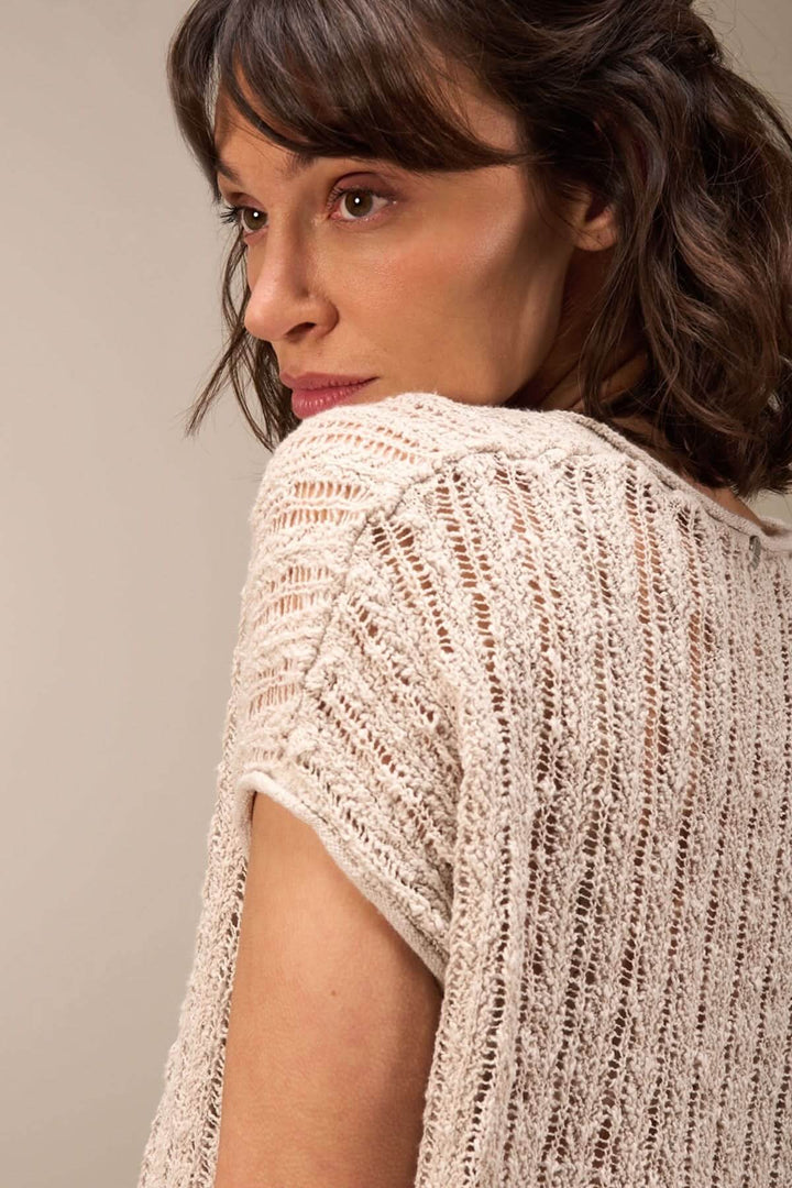 Femme portant un haut en maille ajourée, montrant le dos et les manches courtes, style décontracté et estival.