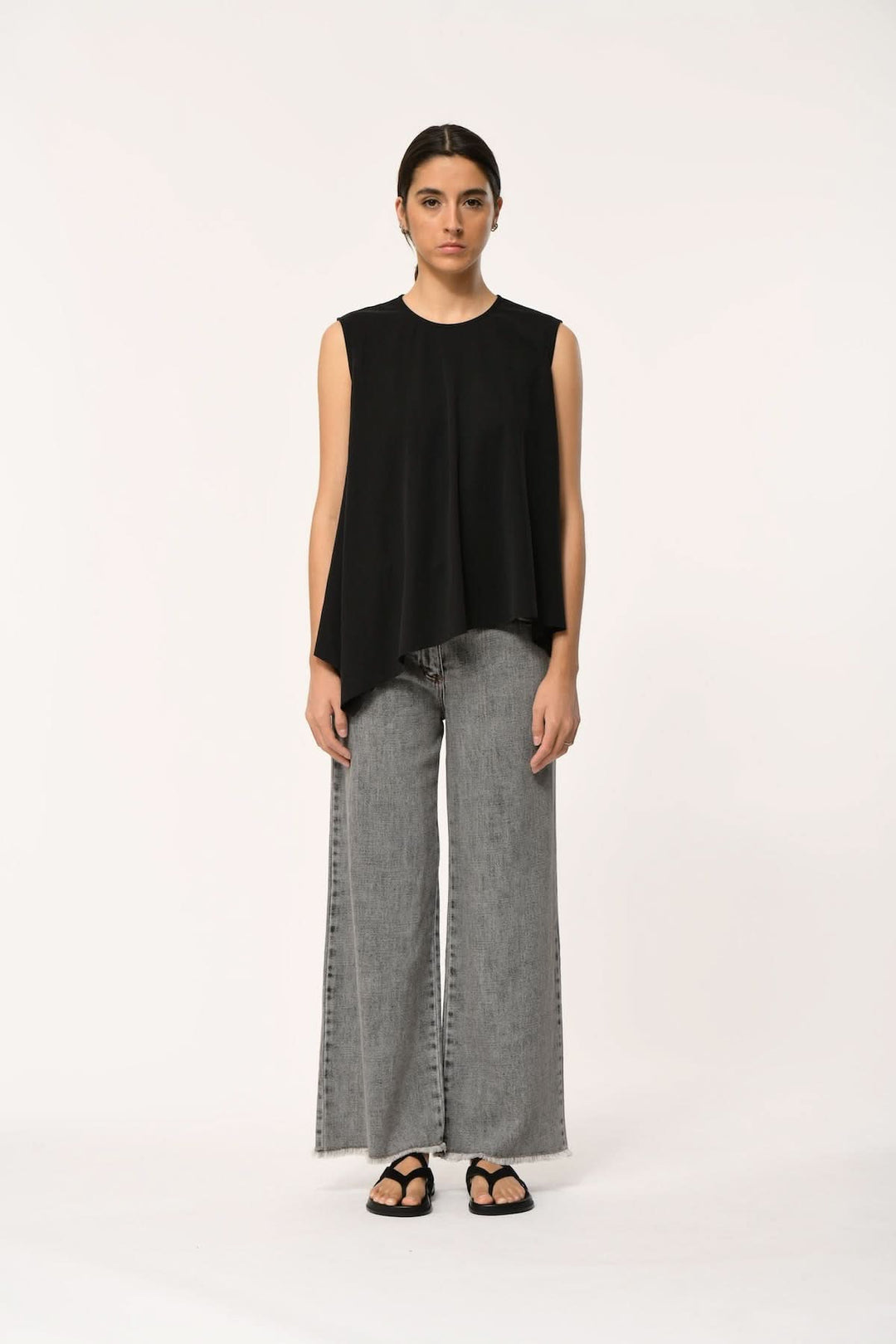 Haut fluide LORO asymétrique sans manches porté avec un pantalon en jean pour un look moderne et élégant.