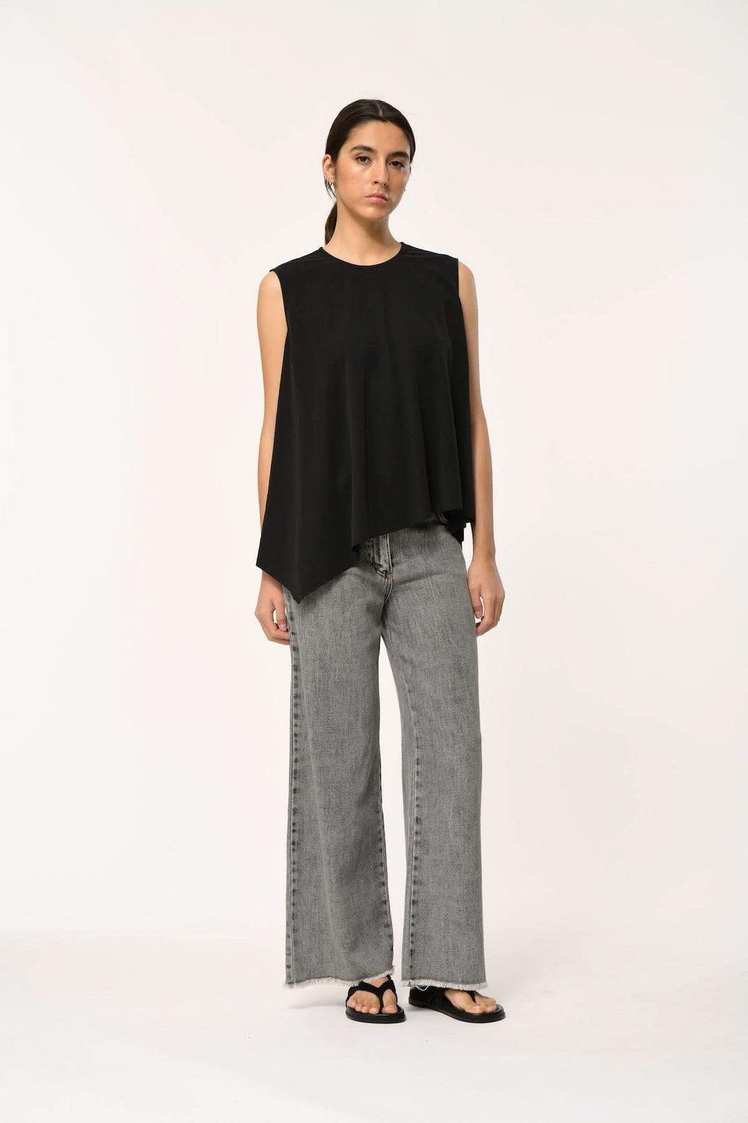 Modèle portant un haut fluide LORO asymétrique sans manches noir avec jean gris moderne.