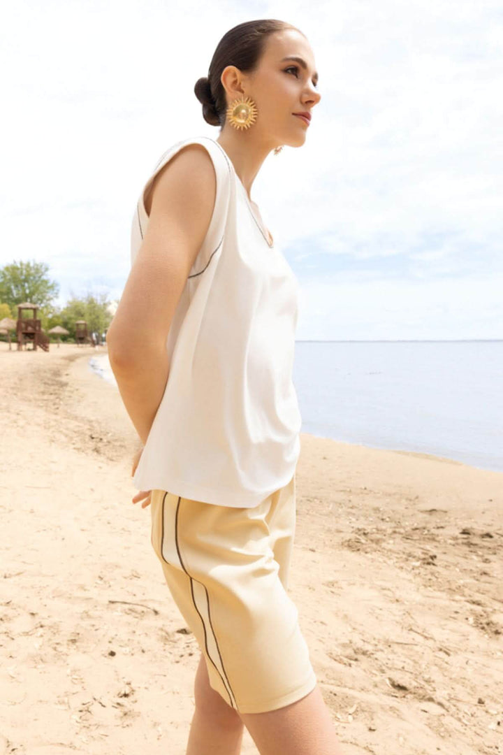 Femme portant haut fluide col en V avec finitions apparentes, bord de mer, style élégant et moderne.