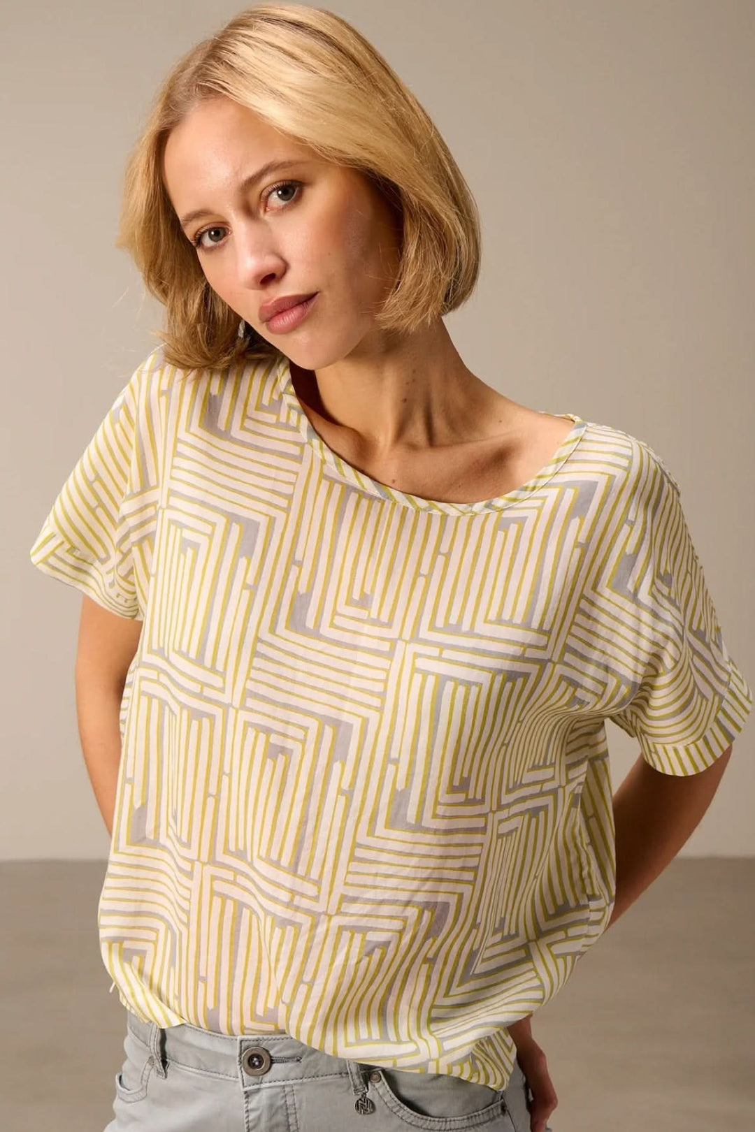 Femme portant un haut fluide imprimé manches courtes avec motifs graphiques, parfait pour un style polyvalent et moderne.