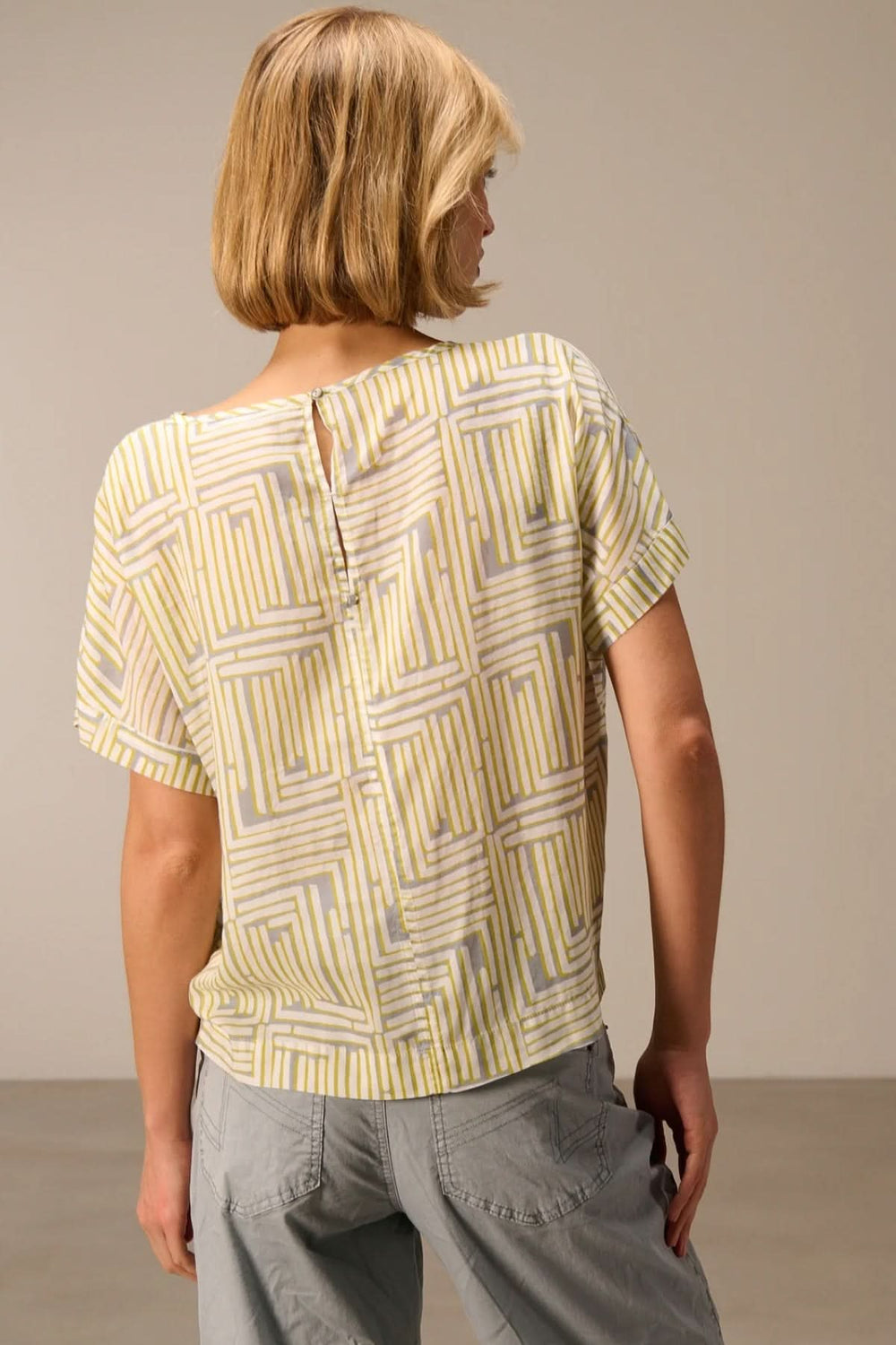 Haut fluide imprimé manches courtes avec motif graphique moderne vue de dos, porté avec un pantalon décontracté.