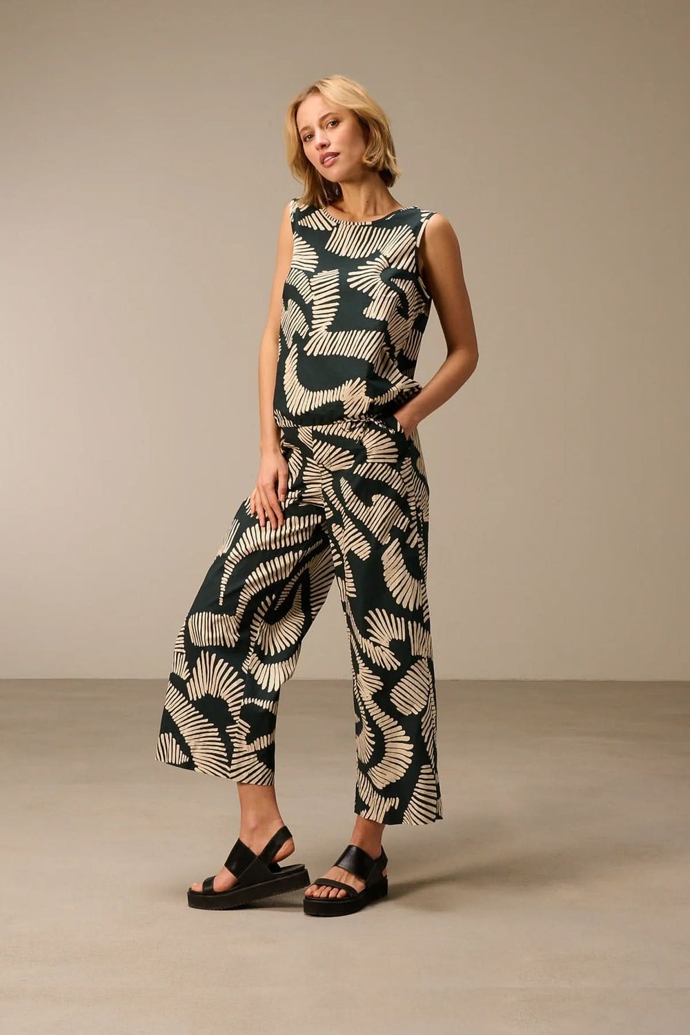 Femme portant un haut fluide sans manches imprimé, silhouette contemporaine et confortable.