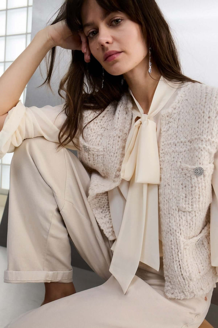 Femme portant un haut sans manches en maille douce dans un style moderne et raffiné, assise en tailleur, avec une chemise élégante.