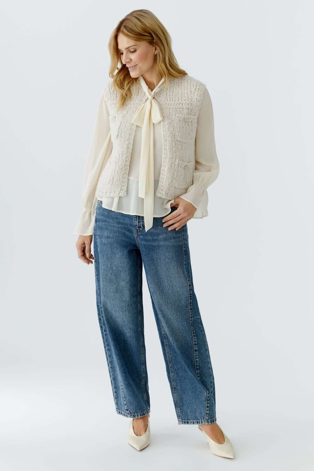 Femme portant un haut sans manches en maille sur une chemise, avec un jean et des talons crème.