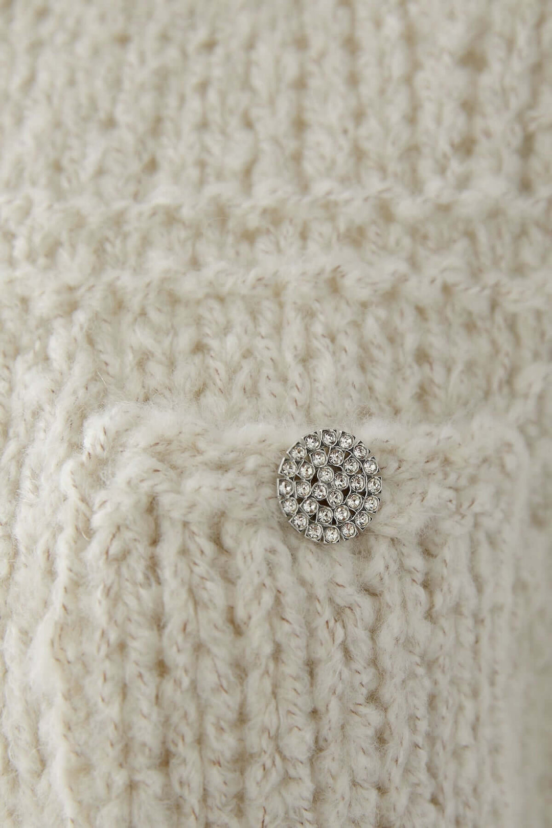 Détail du haut sans manches en maille doux avec un bouton décoratif argenté.