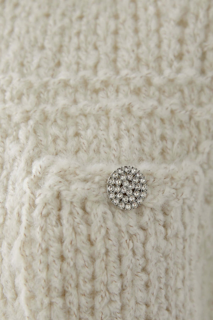 Détail du haut sans manches en maille doux avec un bouton décoratif argenté.