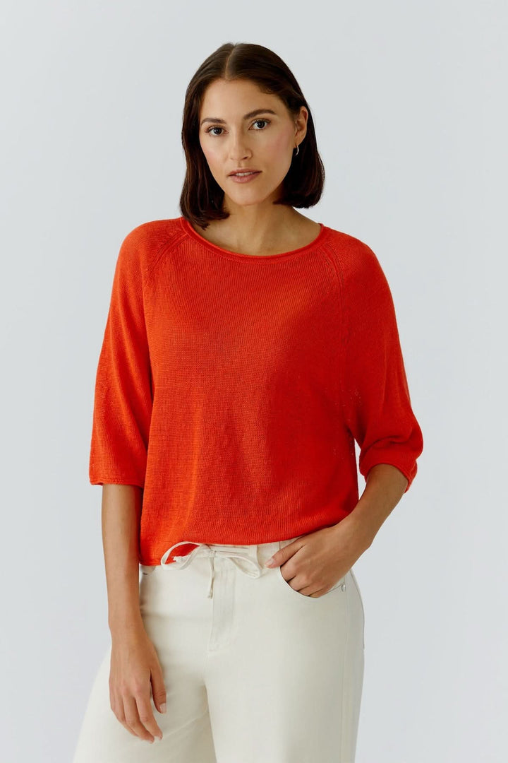 Femme portant un haut texturé minimaliste rouge avec encolure classique et manches trois-quarts, parfait pour bureau et sorties.