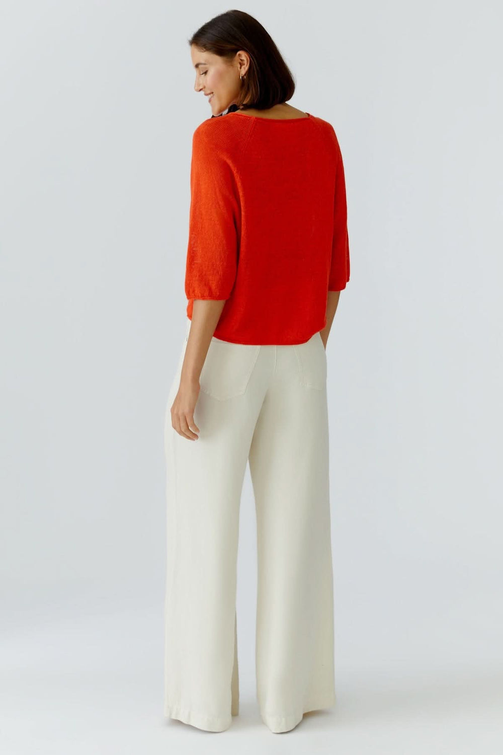 Femme portant un haut texturé minimaliste avec pantalon blanc, vue de dos.
