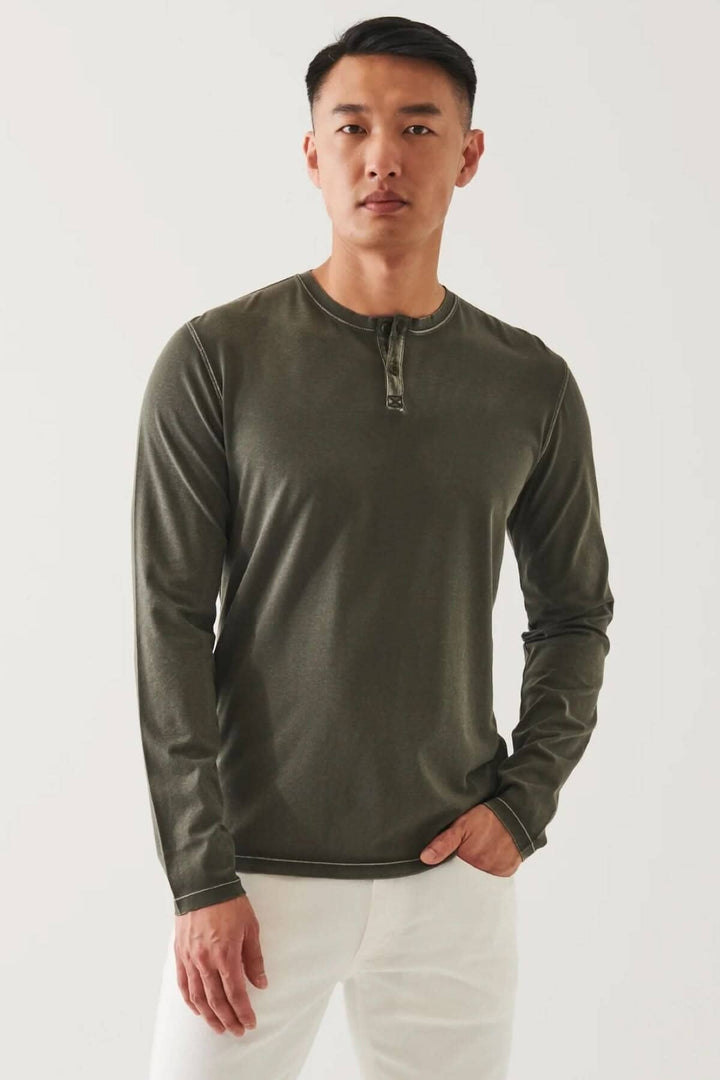 Henley en coton stretch vintage wash, à manches longues, couleur olive, porté avec un pantalon blanc.