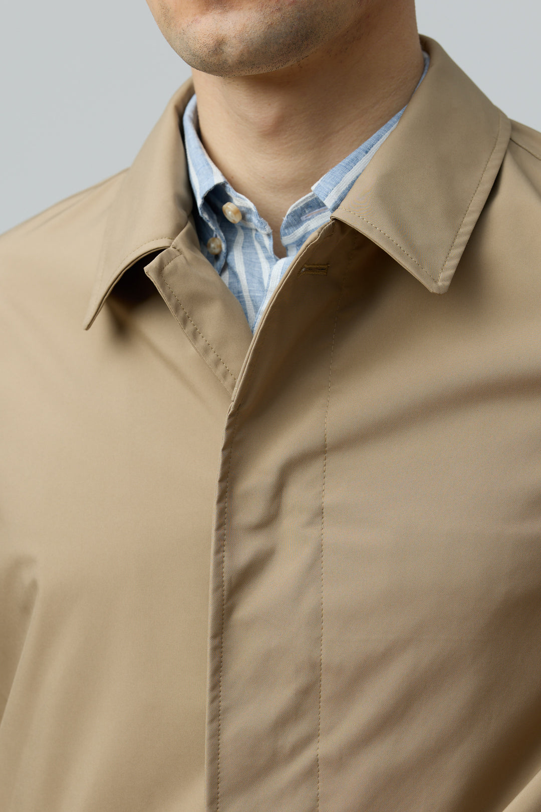 Homme portant un imperméable en microfibre technique au fini ultra-mat avec col chemise et détail de fermeture boutonnée.