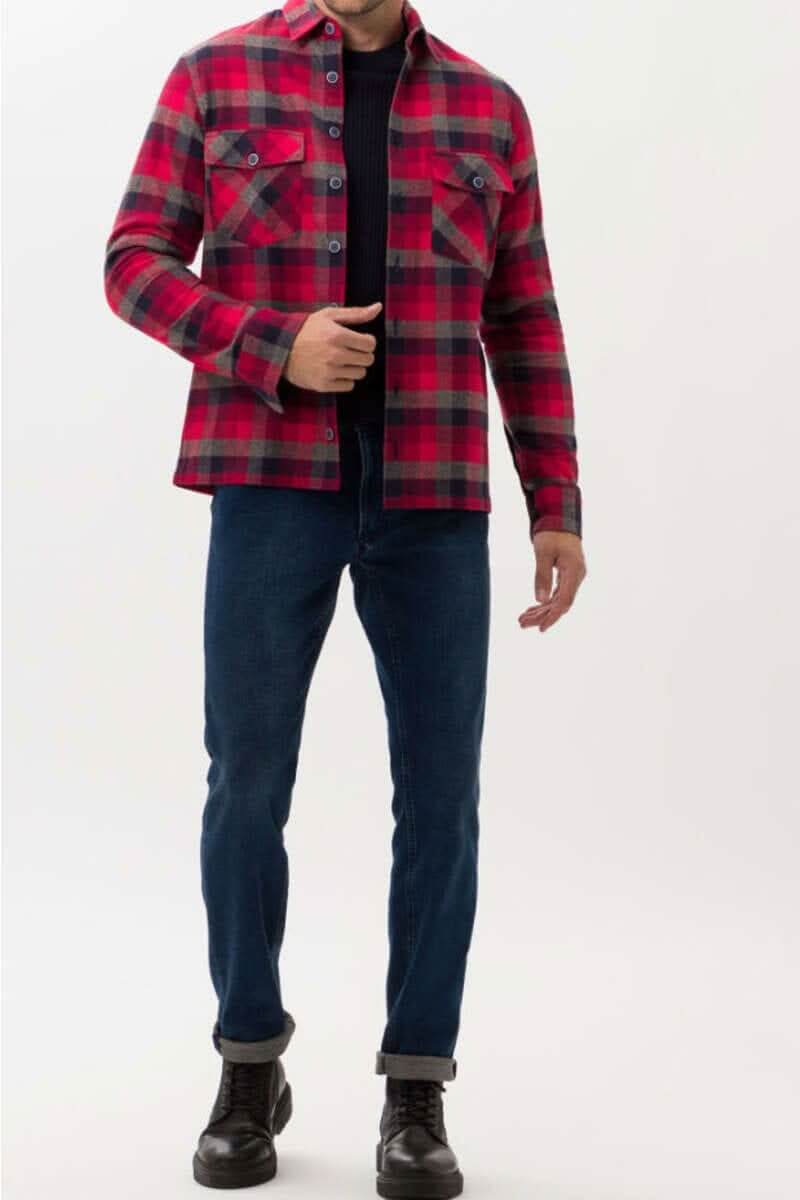 Homme portant une chemise à carreaux rouge et noir avec un pantalon bleu, créant un look décontracté et stylé.