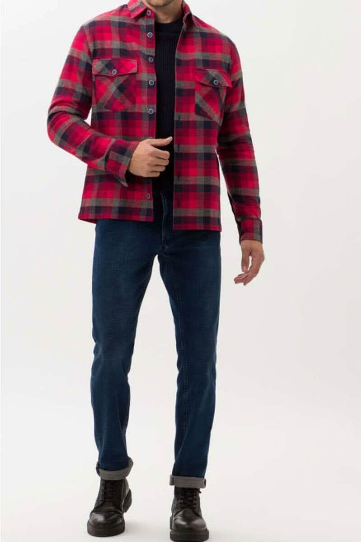 Homme portant une chemise à carreaux rouge et noir avec un pantalon bleu, créant un look décontracté et stylé.