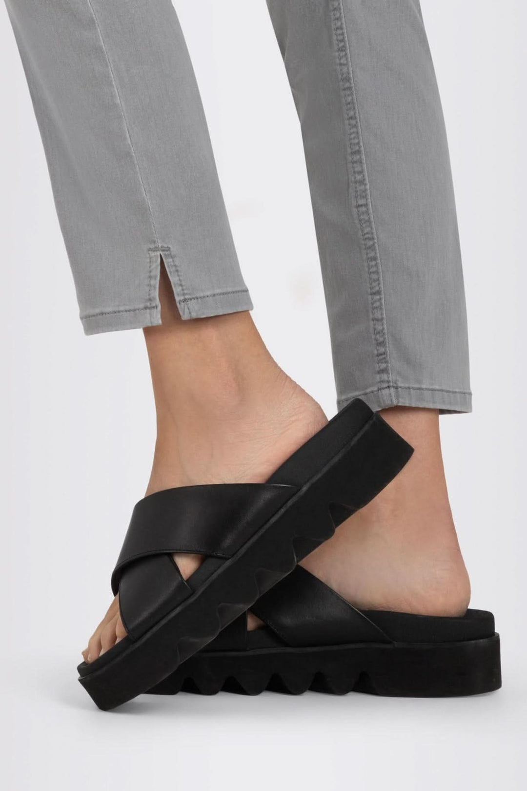 Sandales noires confortables avec design croisé, portées avec un jean gris à détail fendu à l'ourlet.