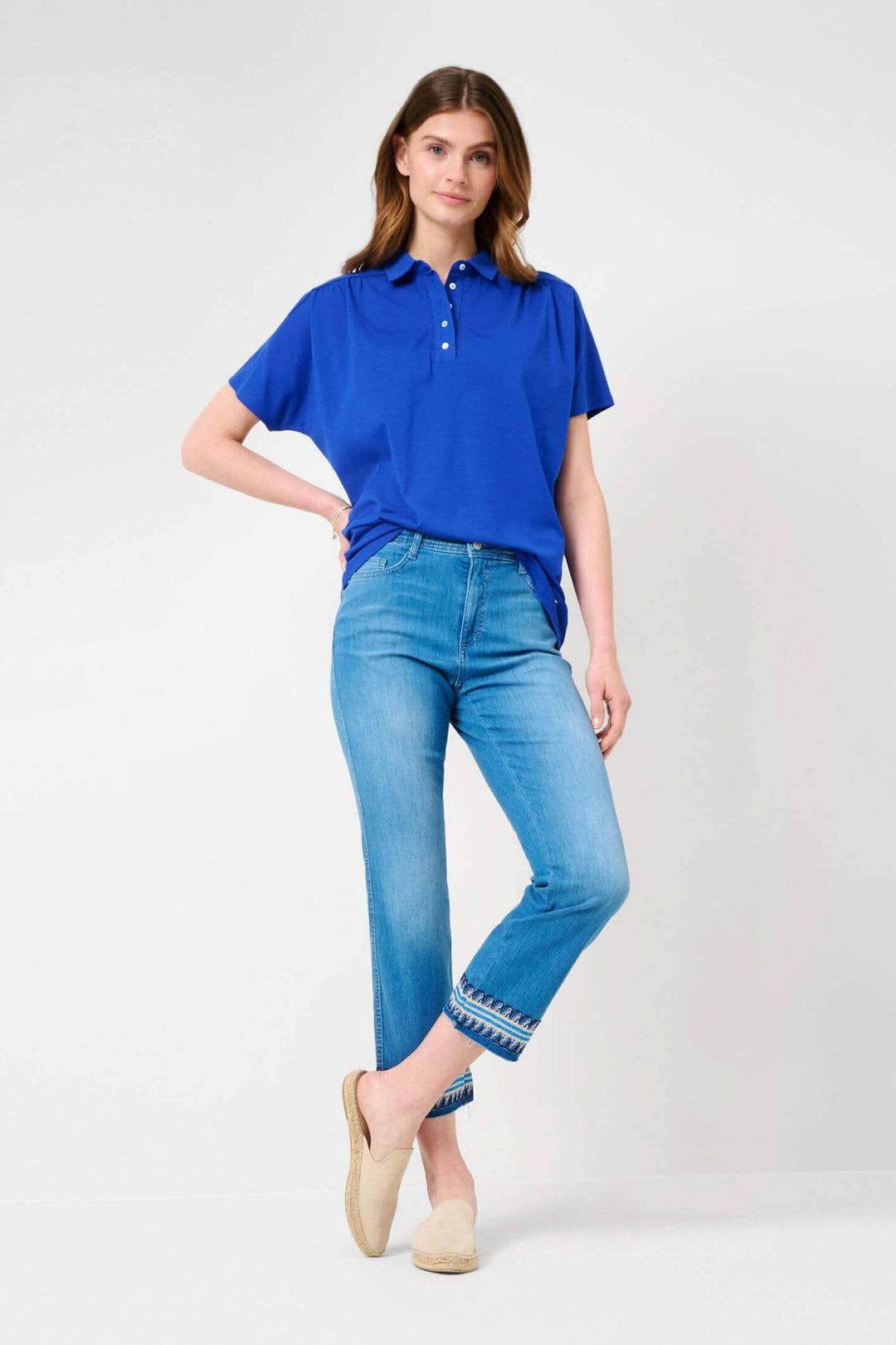 Femme portant un polo bleu et un jean 6/8 avec broderie au bas, style décontracté et élégant.