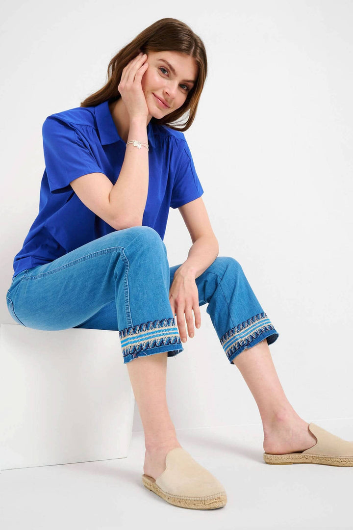 Femme souriante portant un t-shirt bleu avec un jean brodé style bootcut à cinq poches.