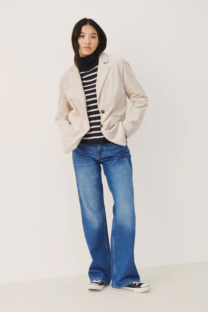 Modèle portant un blazer beige, un pull rayé et un jean bleu, style décontracté et moderne.