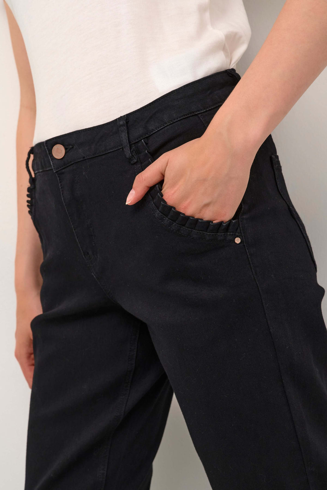Jean à jambe droite noir avec poches obliques et détail plissé, porté avec un haut blanc.
