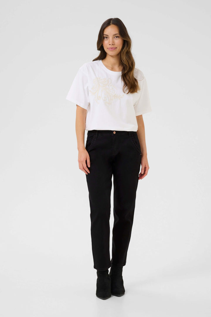 Femme portant un t-shirt blanc et un jean noir à jambe droite, style moderne avec poches ornées.