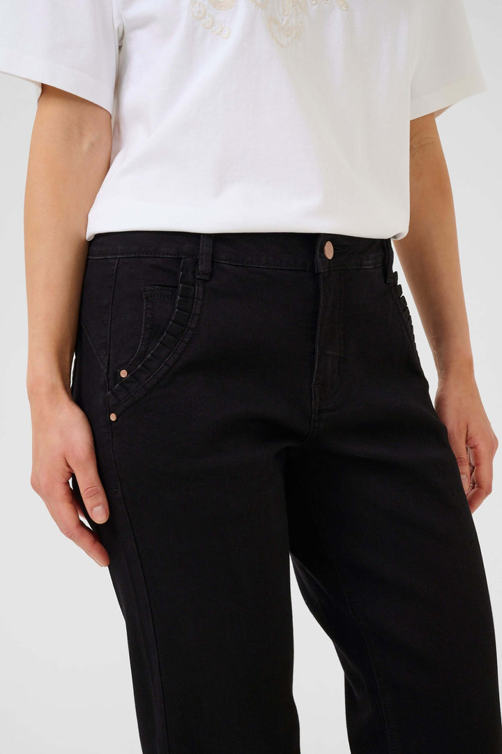 Jean à jambe droite noir avec poches obliques et détail plissé, porté avec un t-shirt blanc.