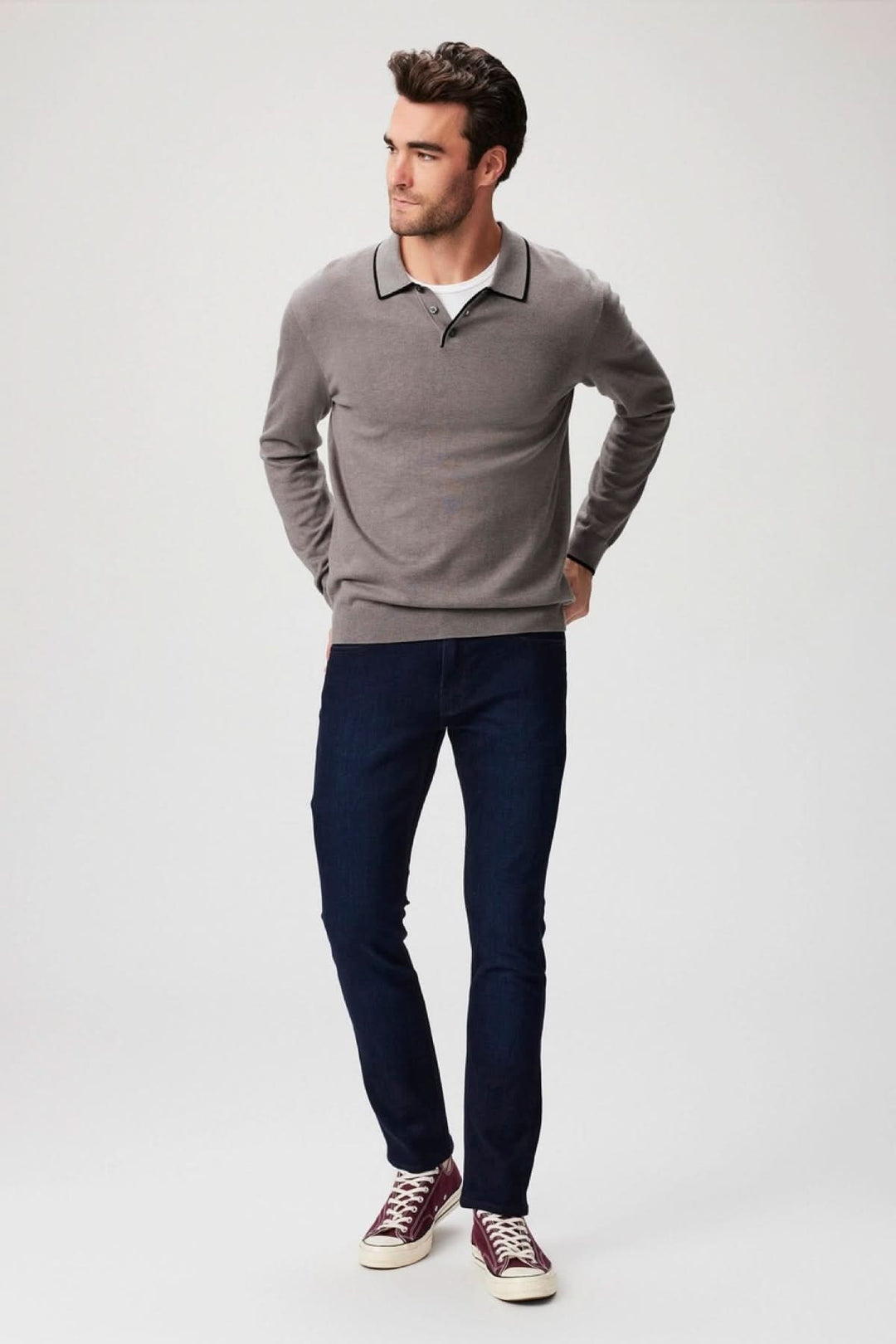 Homme portant un pull gris et un jean slim bleu, complet avec des baskets bordeaux, dans un style décontracté.