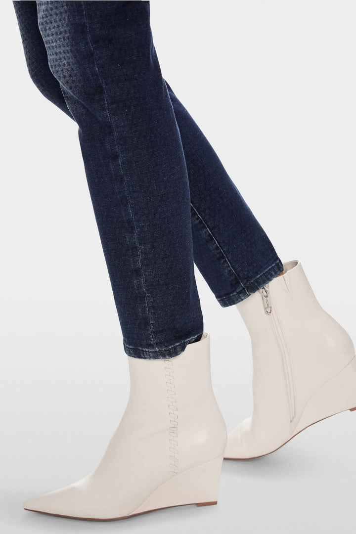 Bottes blanches à talon compensé portées avec un jean slim bleu foncé, mettant en avant un look élégant.
