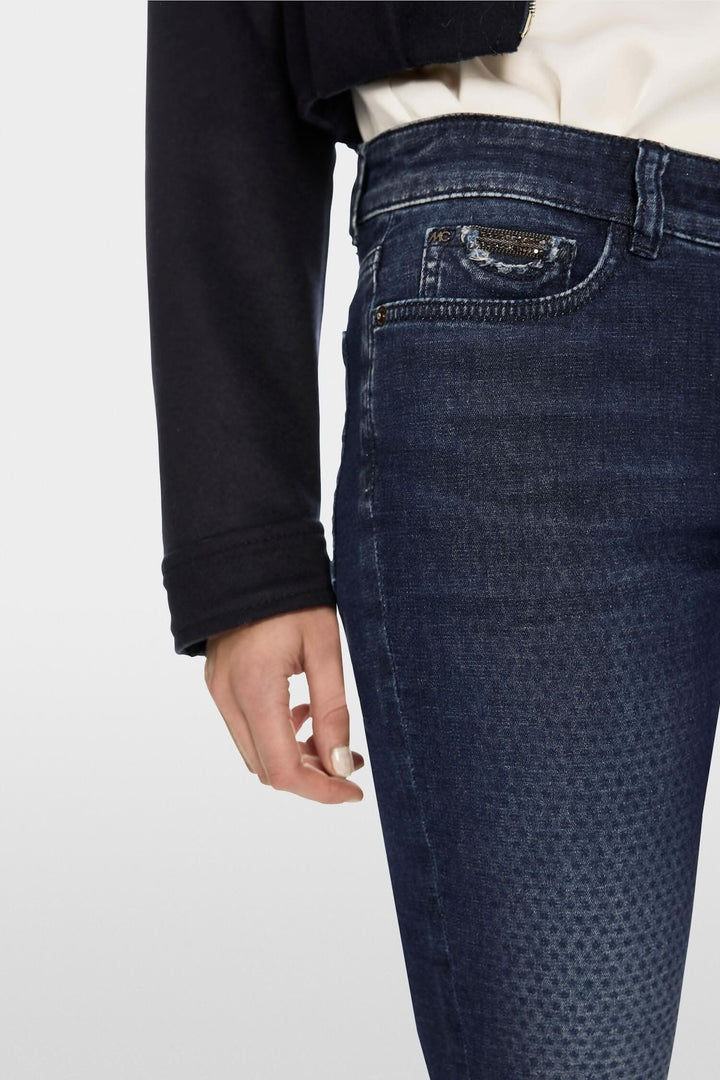 Jean Silvi slim fit avec détails de quadrillage foncé sur un fond bleu, porté avec un pull noir.