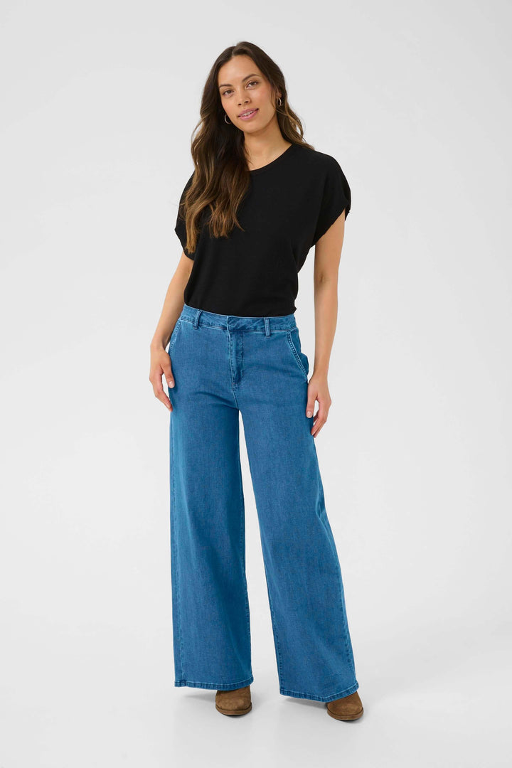 Femme portant un jean à jambe large bleu, t-shirt noir, look décontracté et élégant, taille mi-haute.