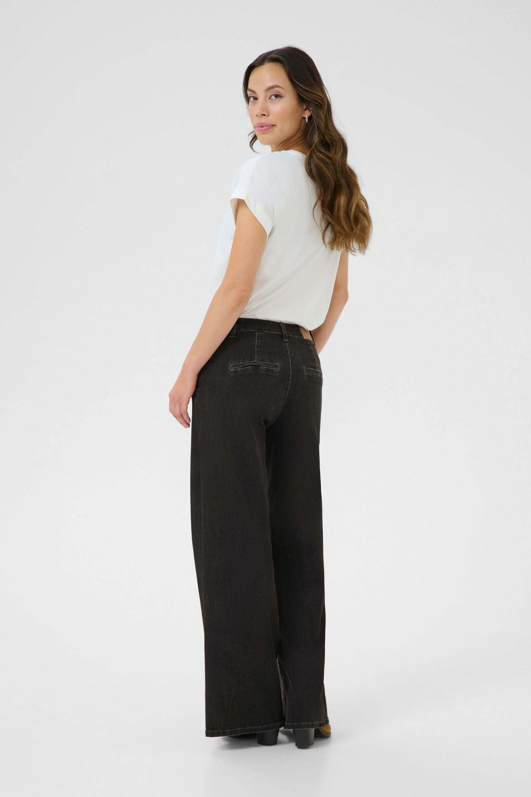 Femme portant un jean large noir à taille mi-haute, avec un t-shirt blanc, vue de dos.