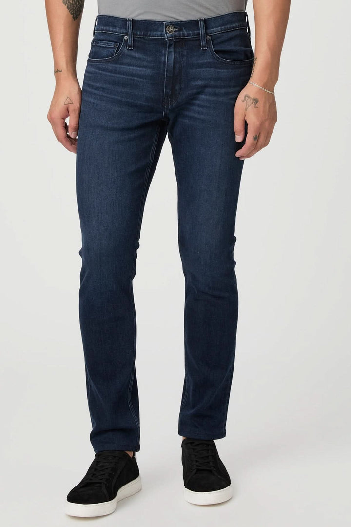 Jean ajusté vintage en délavage foncé, coupe classique, porté avec des sneakers, style décontracté chic.