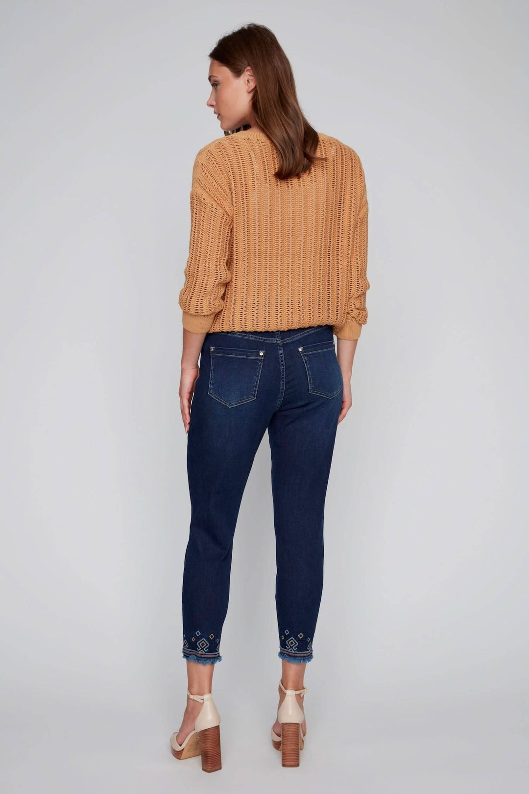 Jean à jambe droite avec broderies géométriques colorées, porté avec un pull beige à col rond.