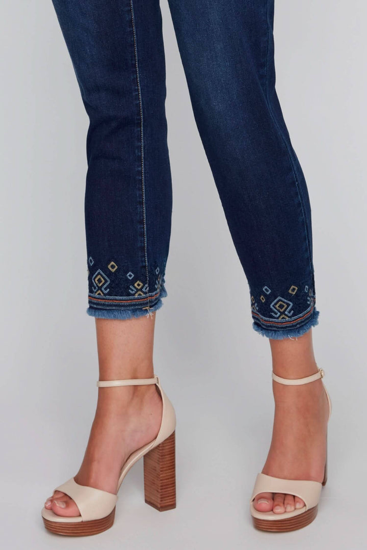 Jean bleu avec broderies géométriques aux chevilles, associé à des sandales à talons beiges.