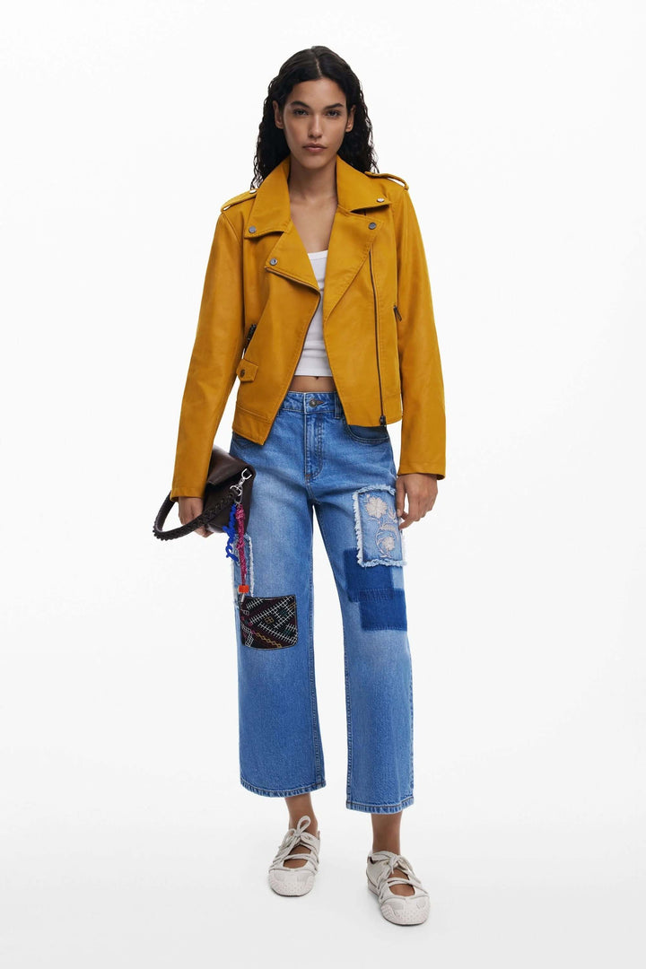 Jean à broderies avec empiècements contrastants et coupe large, porté avec une veste jaune et un t-shirt blanc.