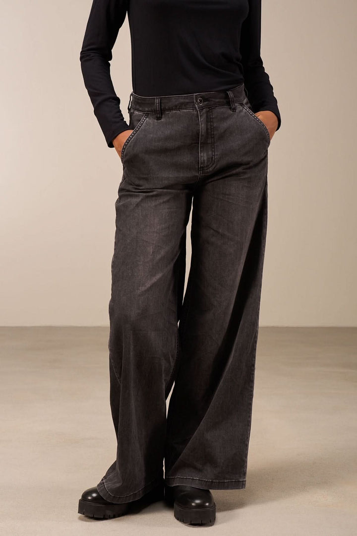 Femme portant un jean coupe large noir avec taille mi-haute et jambes amples, style décontracté et élégant.