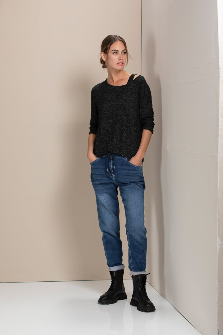 Femme portant un jean décontracté, coupe droite et ample, avec un chandail gris et des bottes noires, illustrant un style moderne et confortable.