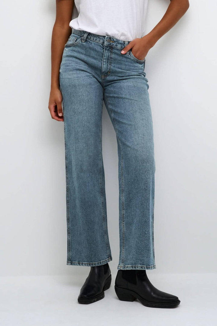 Jean droit Dana en denim bleu, coupe straight, portée avec un t-shirt blanc et des bottines noires.