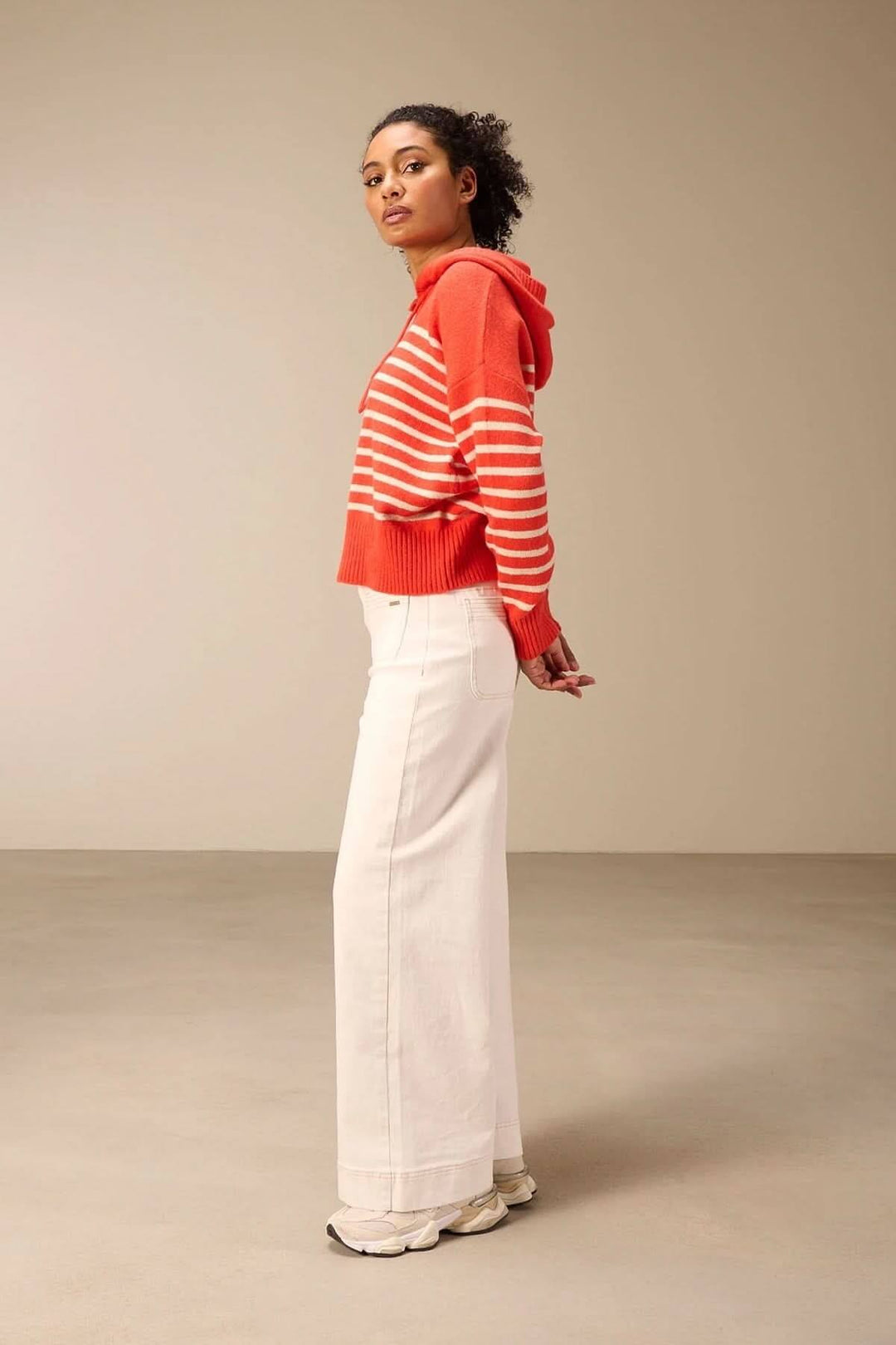 Jean jambe large blanc avec taille haute, porté avec un pull rayé rouge, offrant un look rétro moderne et confortable.