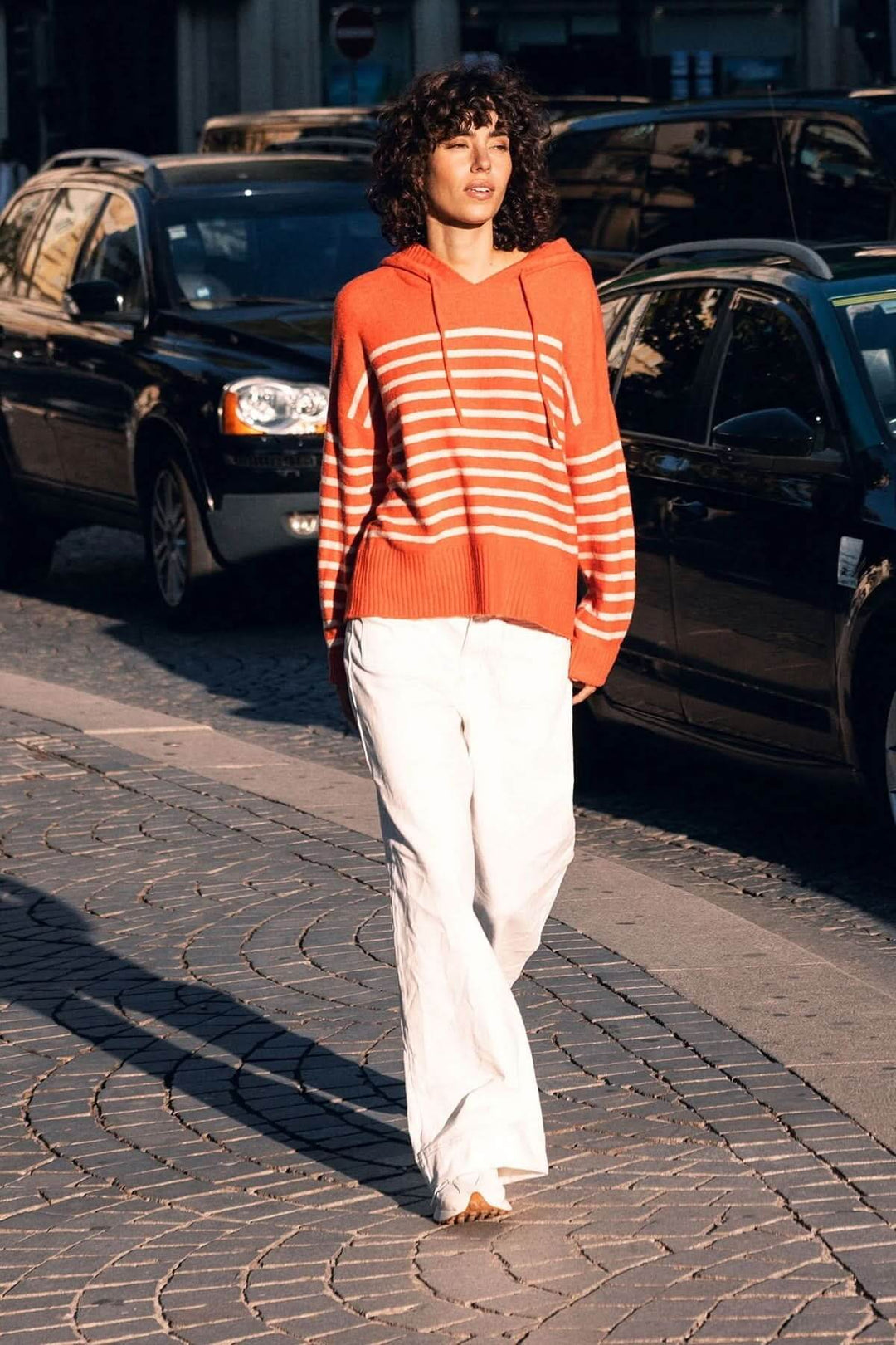 Femme portant un jean jambe large blanc avec un pull rayé orange, marchant en extérieur. Le jean à taille haute offre un confort naturel.