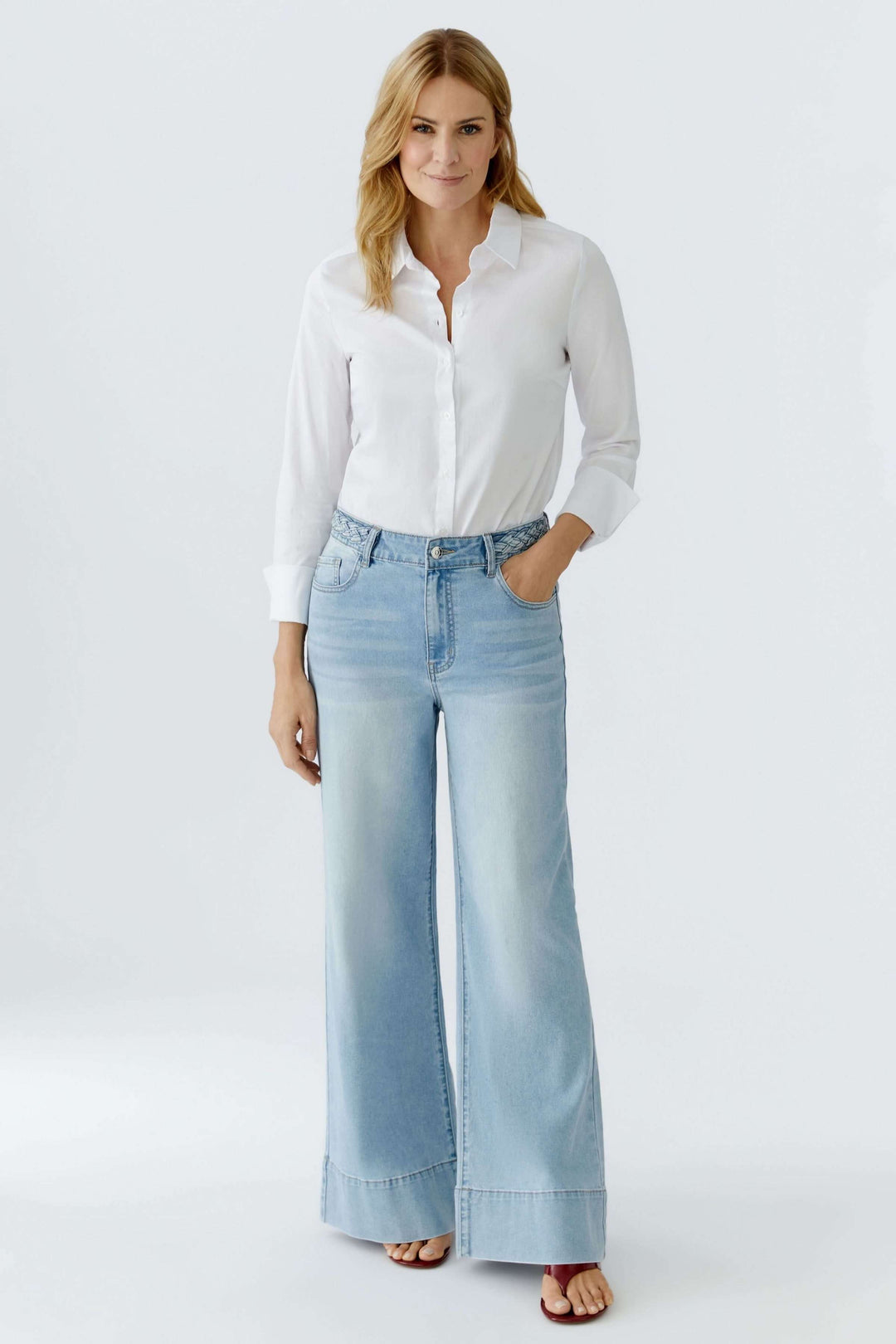 Jean à jambe large avec taille tressée en denim, porté avec une blouse blanche. Silhouette moderne et détail élégant.
