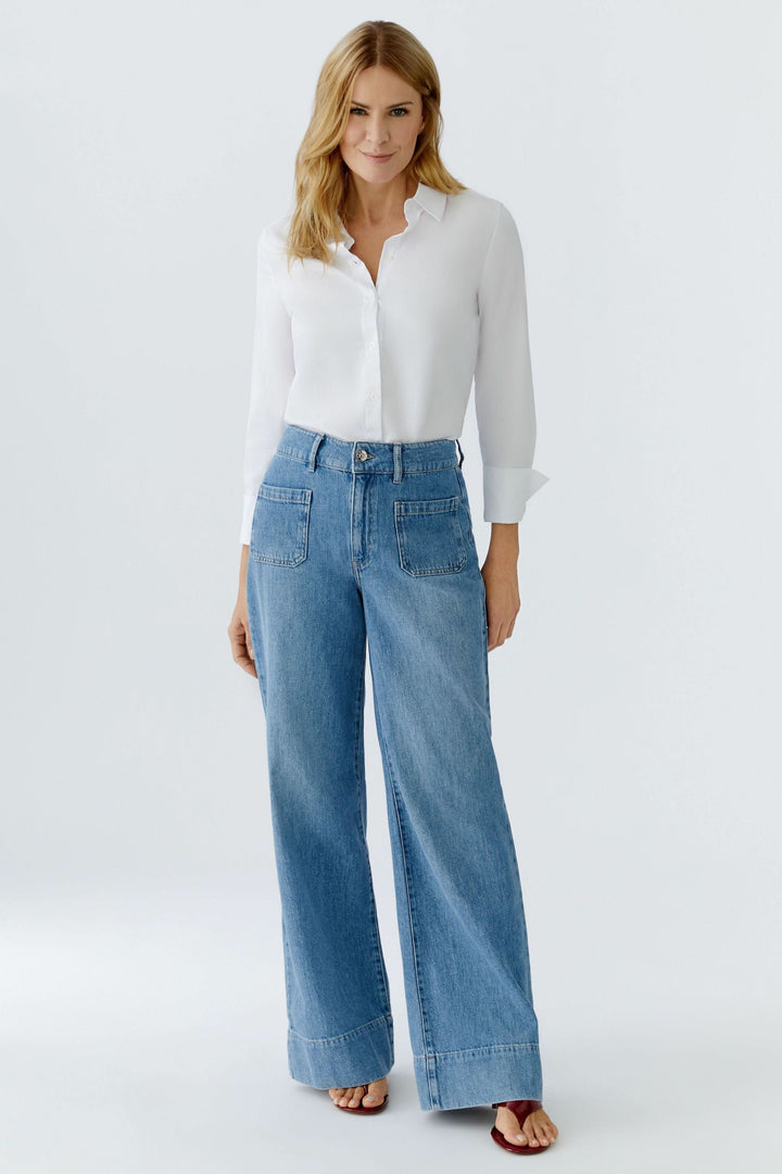 Jean large à taille haute porté avec une blouse blanche, mettant en valeur la taille avec une coupe fluide et moderne.