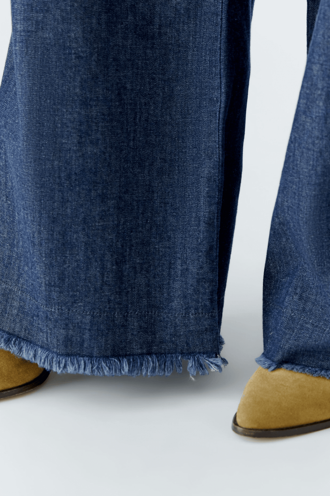 Jean ultra léger avec coupe large, longueur normale et franges aux ourlets, porté avec des bottines beiges.