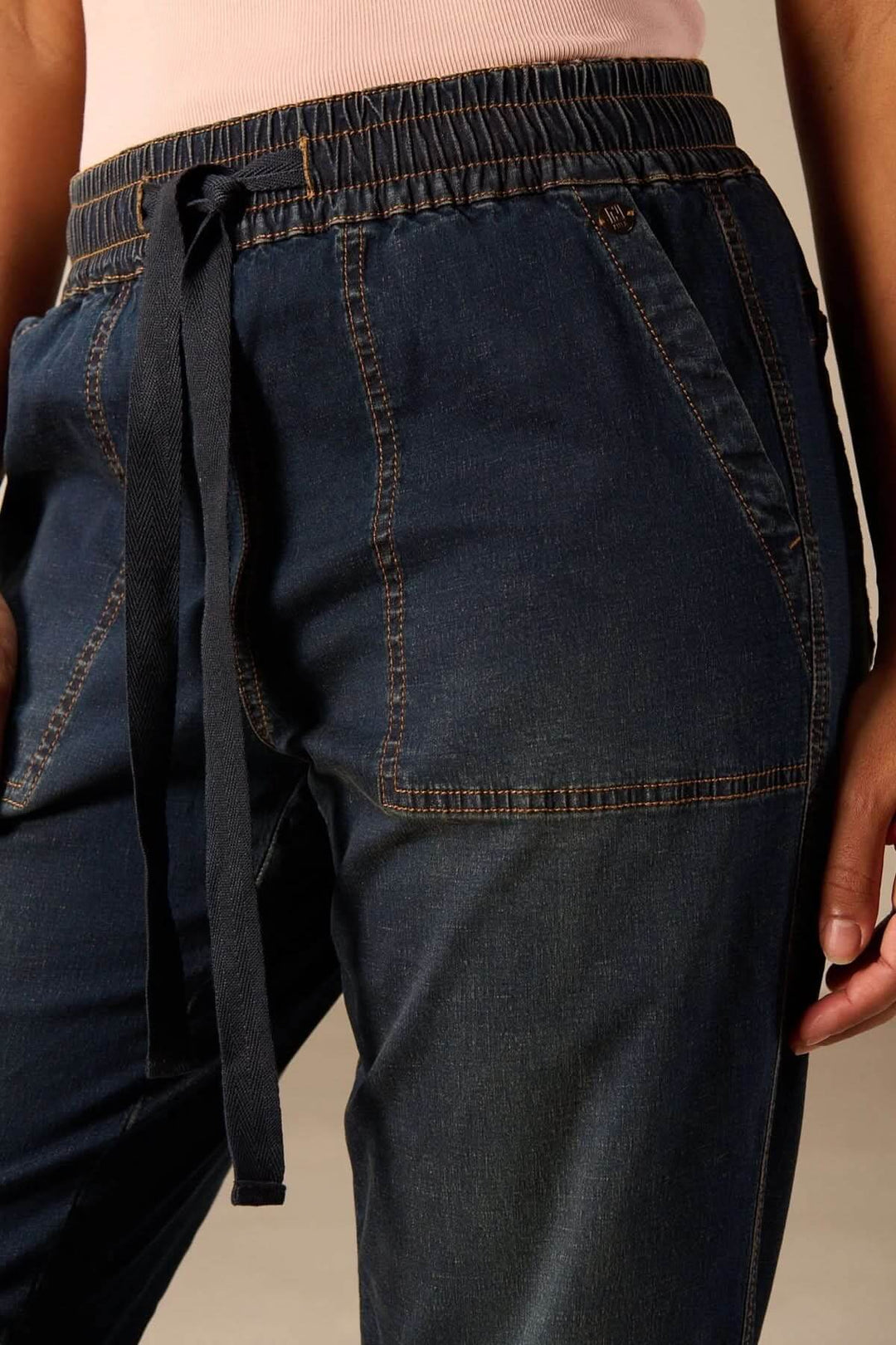 Gros plan sur jean jogging à taille élastique avec cordon ajustable et coupe fuselée, offrant style décontracté et confort.