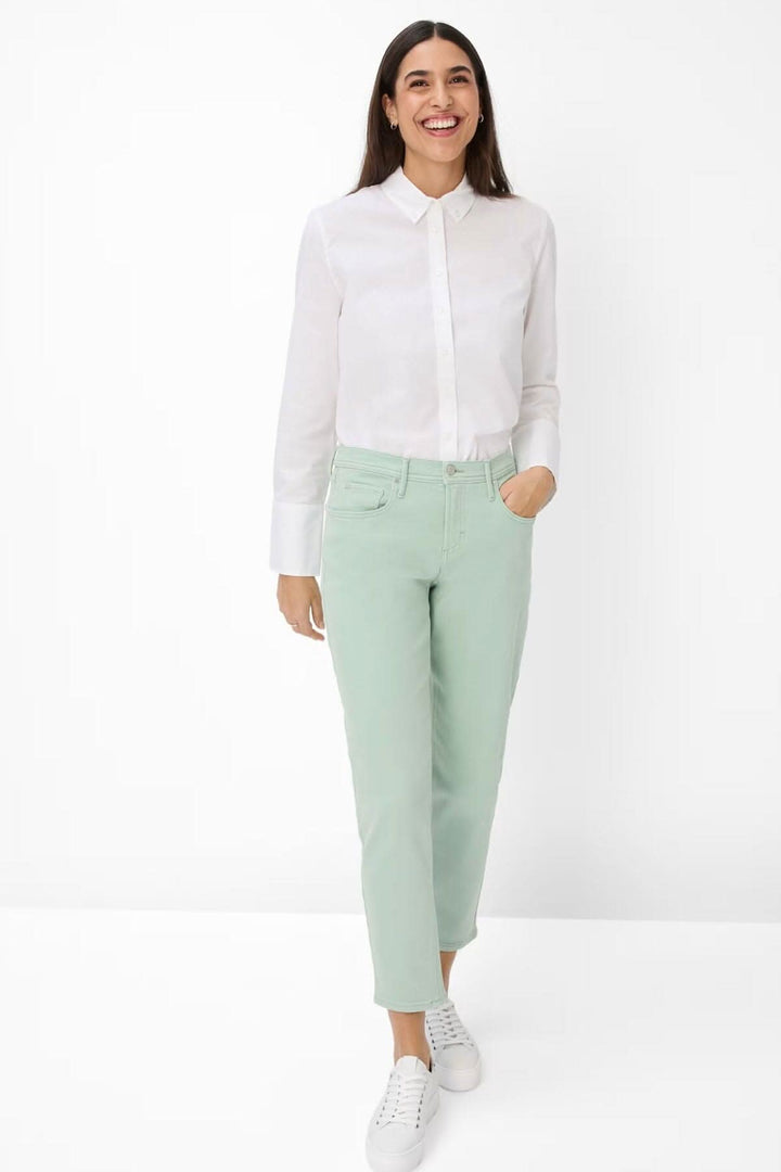 Femme souriante portant une chemise blanche et un pantalon vert clair, style décontracté élégant.