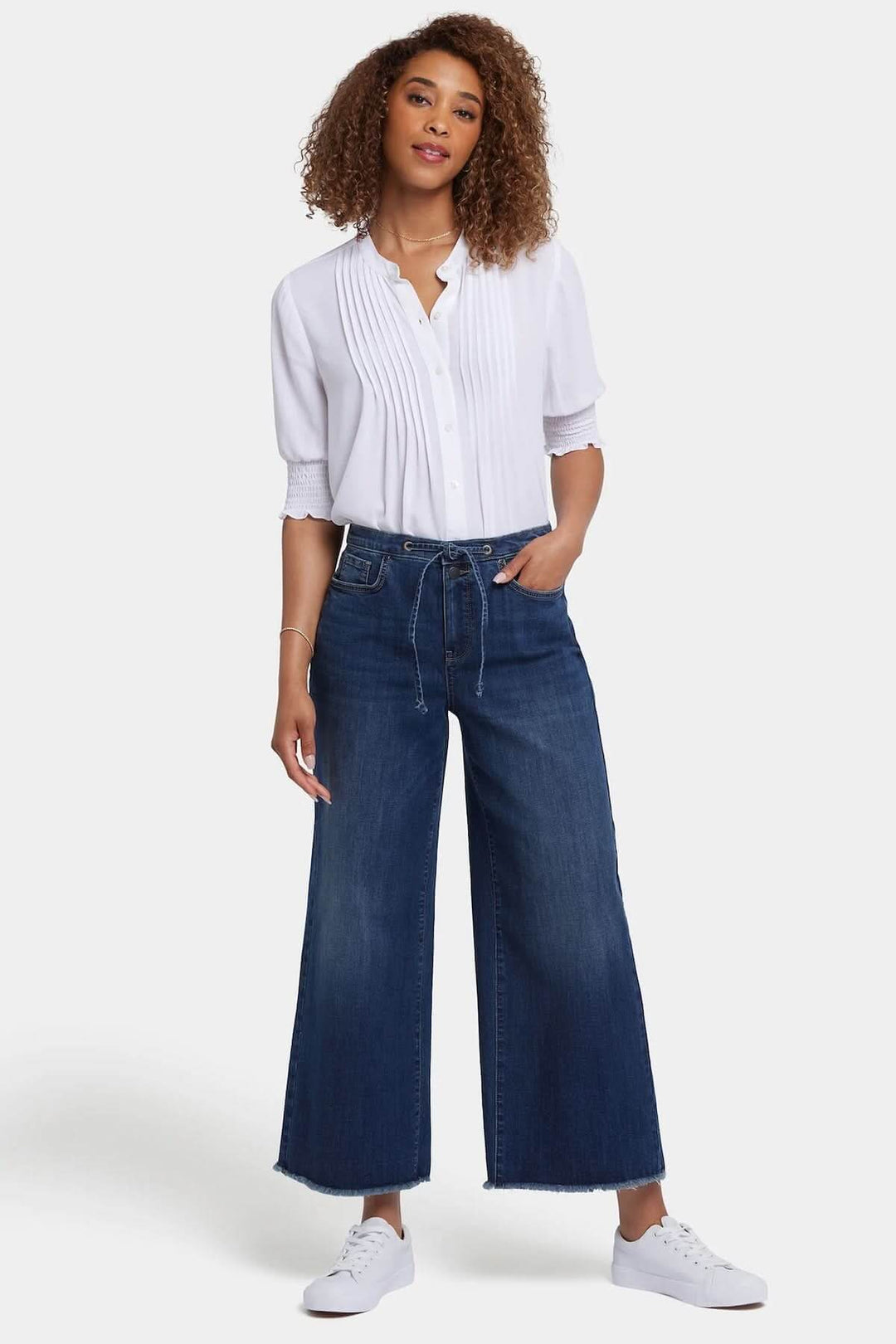 Jeans Cindi à jambe large avec taille haute et cordon ajustable, porté avec blouse blanche et baskets.