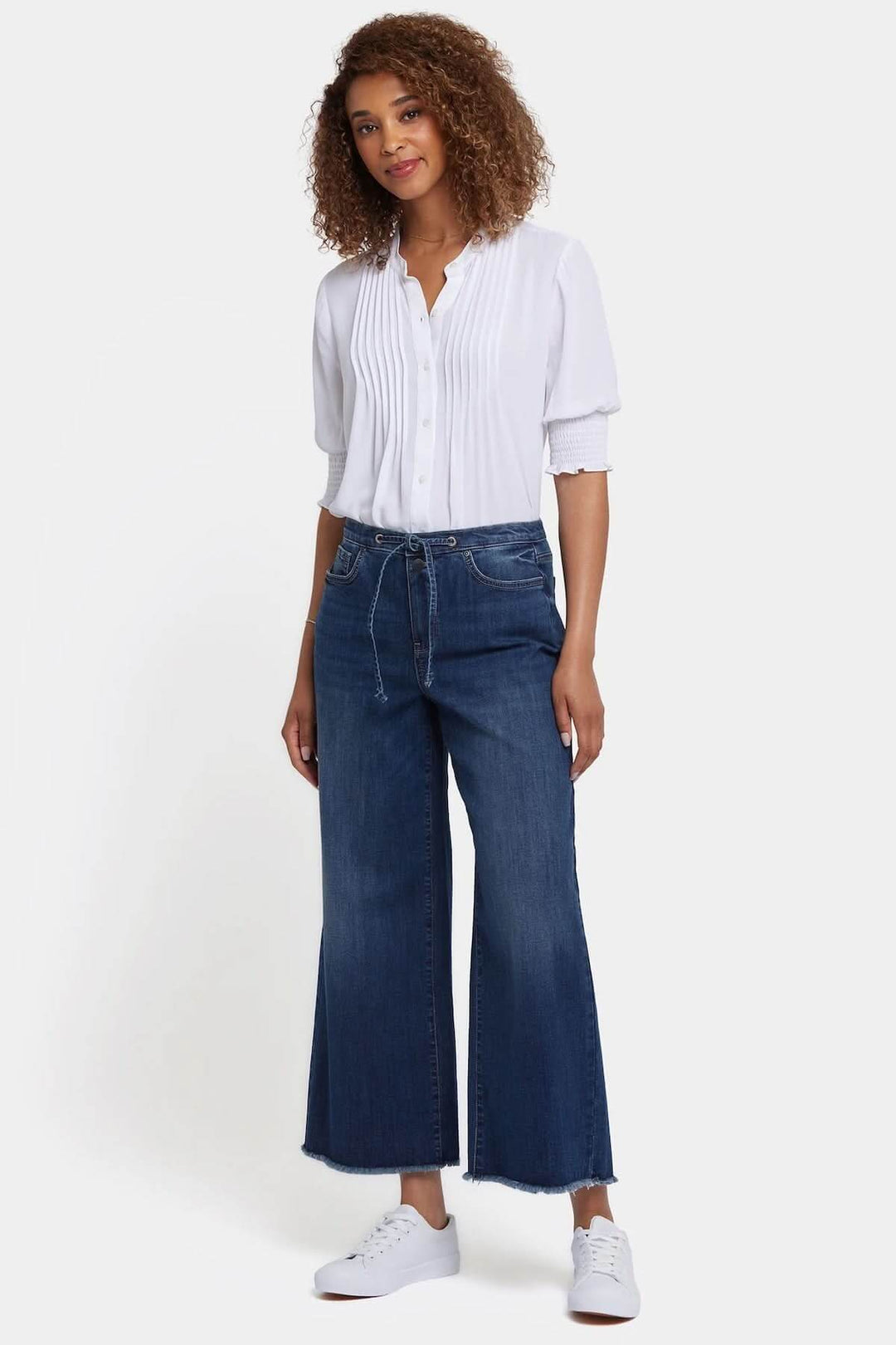 Femme portant des jeans Cindi à jambe large avec taille haute et blouse blanche élégante.