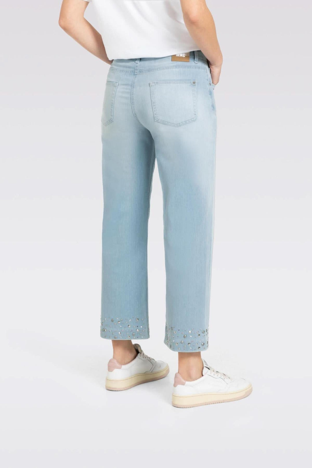 Jean culotte en denim léger, coupe large et jambe raccourcie avec studs brillants au bas, porté avec des baskets.