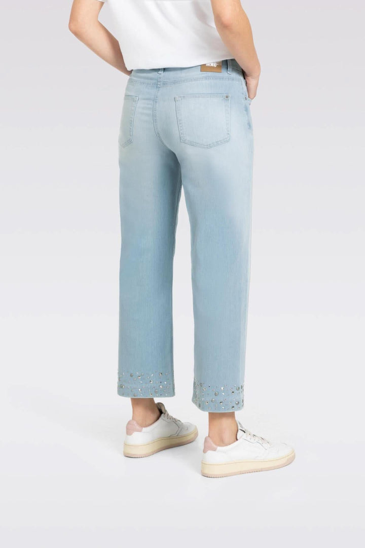 Jean culotte en denim léger, coupe large et jambe raccourcie avec studs brillants au bas, porté avec des baskets.