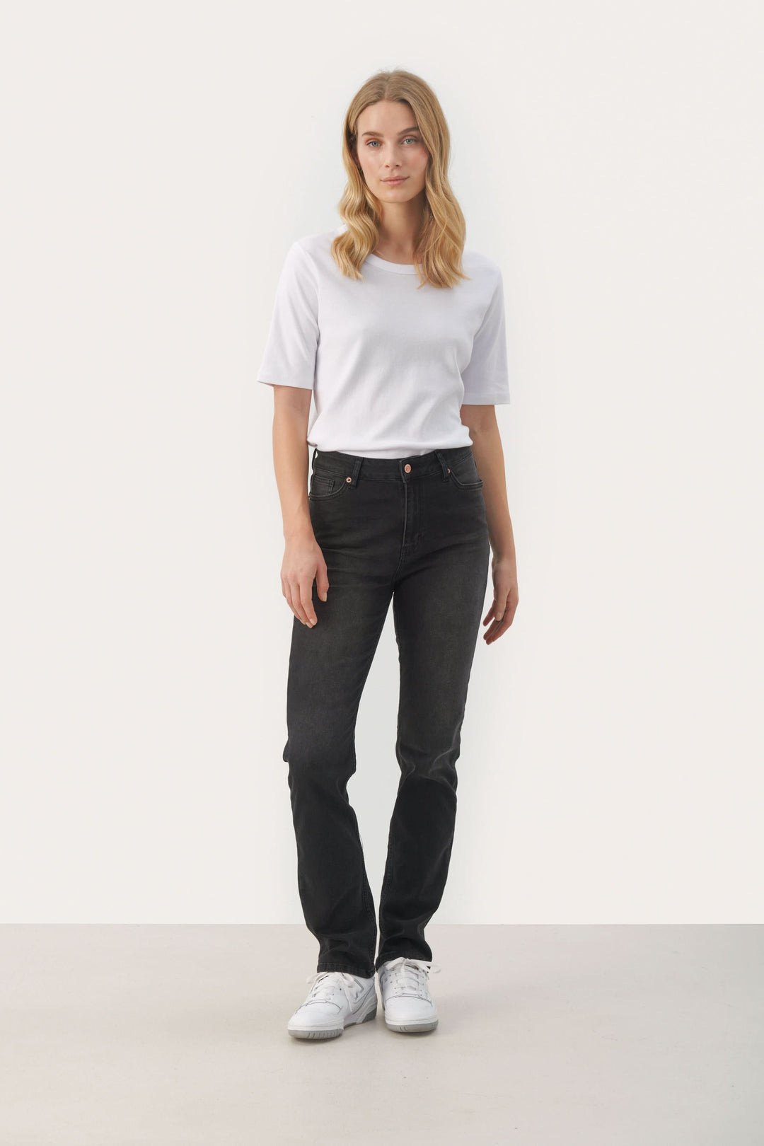 Femme portant des jeans ajustés noirs avec un t-shirt blanc et des baskets, style moderne et décontracté.