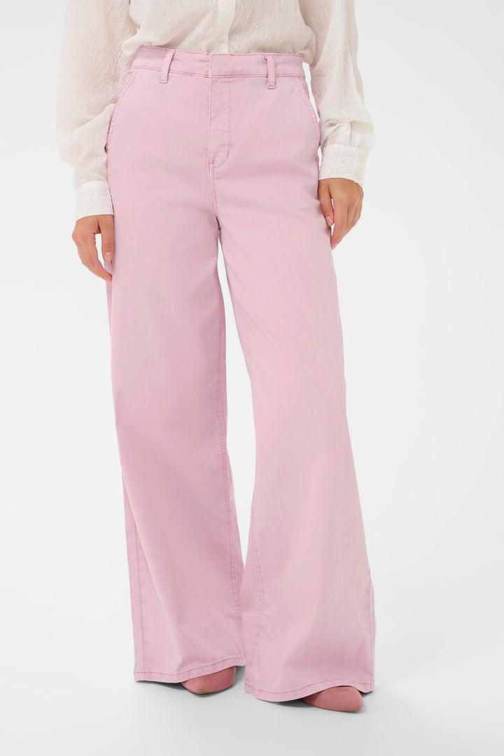 Jeans Visti rose à jambe large, taille régulière, porté avec une blouse blanche pour un look moderne et élégant.
