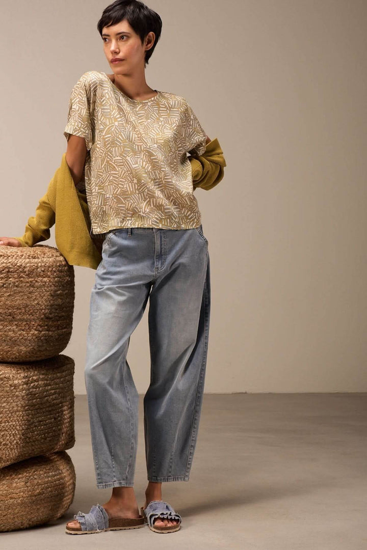 Femme portant un jean ample et un t-shirt imprimé dans un décor décontracté avec des accessoires en osier.